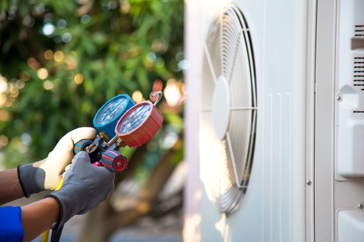 Mechanic air conditioner technician using manifold gauge checking refrigerant for filling home air conditioning and air duct cleaning and maintenance outdoor compressor unit. See Less